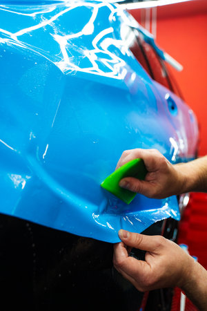 Blue PPF applied with green squeegee during detailing car to preserve finish and block damage. Applying a high-gloss blue PPF using a green squeegee ensures a bubble-free, smooth surface of carの写真素材
