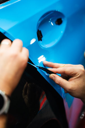 Precision PPF wrapping and detailing on car panel using sharp blade to trim wrap with accuracy. Car detailing involves precise vinyl cutting techniques. Precision cutting of PPF wrap on car bodyの写真素材