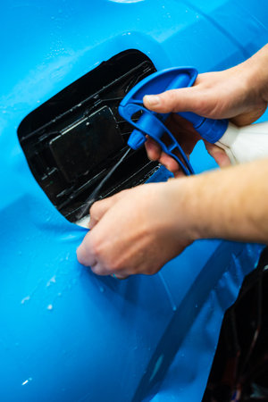 Detailing experts use hydration spray for controlled application of blue PPF film. Detailer uses spray-assisted method to apply vibrant blue vinyl wrap for perfect, bubble-free alignmentの写真素材