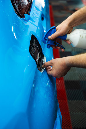 Detailing experts use hydration spray for controlled application of blue PPF film. Detailer uses spray-assisted method to apply vibrant blue vinyl wrap for perfect, bubble-free alignmentの写真素材
