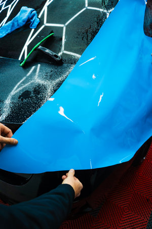 Bold blue vinyl wrap installing in detailing center. Detailers expertly apply wrap to fit contours and ensures smooth, flawless wrap alignment. Applying PPF wrap on car during full detailingの写真素材