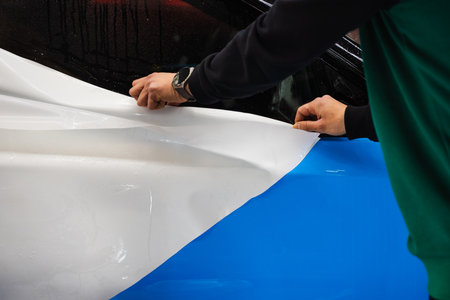 Protective film layering during PPF wrap detailing to protect the car surface from scratches and UV. Wet PPF Wrapping on Car Panel in detailing centerの写真素材