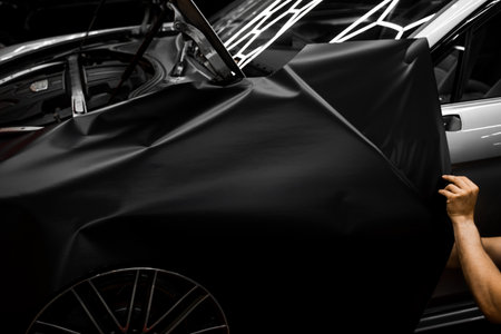 Car Door Panel Wrapping. Process of wrapping car with matte black vinyl and tensioning the material. Car wrapping starts with aligning matte black vinyl to achieve seamless coverageの写真素材