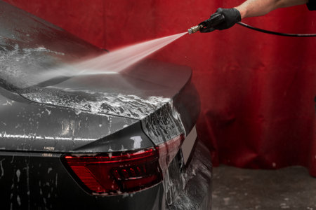 Detailed cleaning using pressure hose ensures no foam or dirt on car. Soapy water is blasted away using jet washer to reveal clean finish. Pressure Rinsing Car After Foam Applicationの写真素材