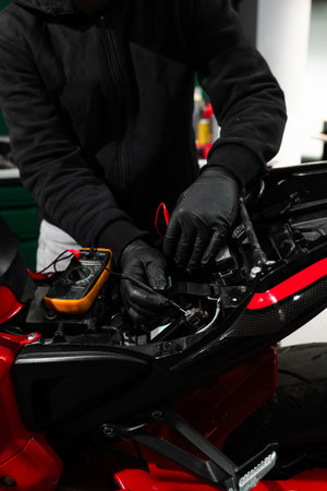 Mechanic testing battery with multimeter. Motorcycle battery is tested using digital multimeter to check voltage and health. Digital multimeter reads motorcycle battery voltage during inspectionの写真素材