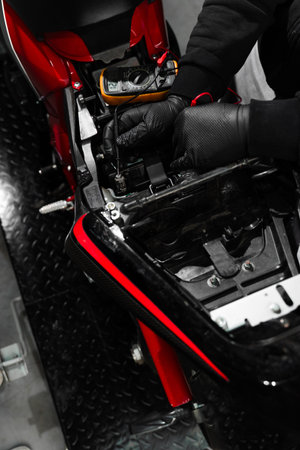 Digital multimeter reads motorcycle battery voltage during inspection. Mechanic testing battery with multimeter. Motorcycle battery is tested using digital multimeter to check voltage and healthの写真素材
