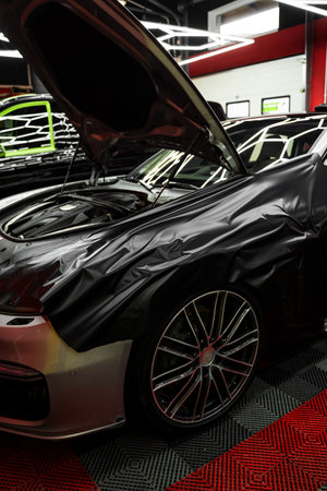 Careful application and tensioning of black vinyl avoids surface damage or bubbling. Matte black vinyl is applied across car hood. Car wrapping process using black matte vinyl stretched into placeの写真素材