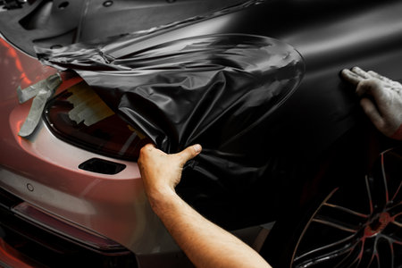 Matte black vinyl wrap application on front fender and wheel arch of luxury vehicle. Vinyl Wrapping of Car. Matte black vinyl wrapping around car with smooth alignment over curves and edgesの写真素材