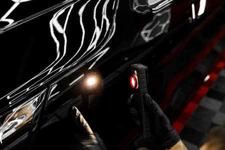 Swirl finder light to detect paint issues on black car in a detailing studio. Car Paint Inspection. Car paint inspection using detailing inspection light before polishing or ceramic coatingの写真素材