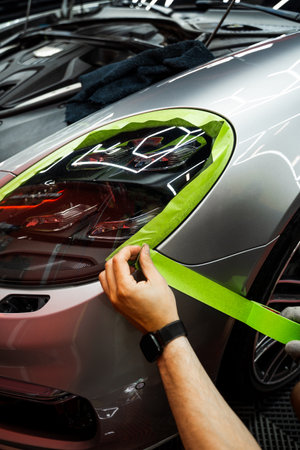 Technician applies masking tape around car panels before installing matte black vinyl wrap. Car Surface Masking for Matte Black Vinyl Wrap Preparationの写真素材