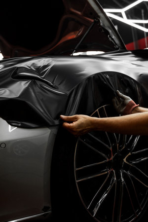 Matte black vinyl wrapping around car with smooth alignment over curves and edges. Matte black vinyl wrap application on front fender and wheel arch of luxury vehicle. Vinyl Wrapping of Carの写真素材