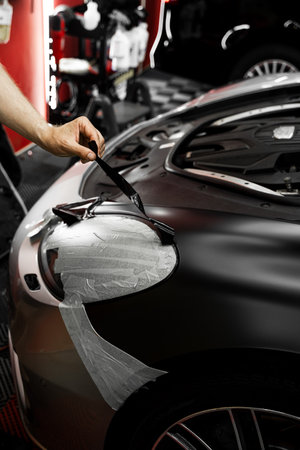 Vinyl film is carefully applied and trimmed with a blade for flawless vehicle wrapping results. Wrapping vinyl requires perfect tension and accurate blade work for high-end detailingの写真素材