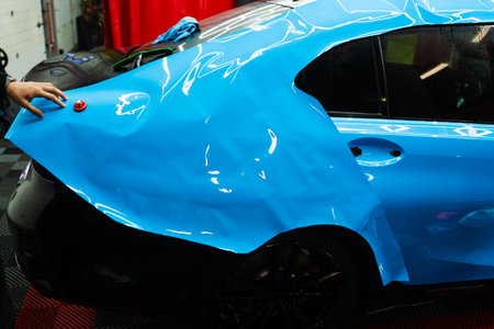 Detailers expertly apply wrap to fit contours and ensures smooth, flawless wrap alignment. Applying PPF wrap on car during full detailing. Bold blue vinyl wrap installing in detailing centerの写真素材