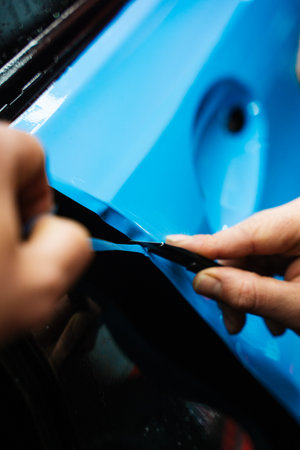 Precision PPF wrapping and detailing on car panel using sharp blade to trim wrap with accuracy. Car detailing involves precise vinyl cutting techniques. Precision cutting of PPF wrap on car bodyの写真素材