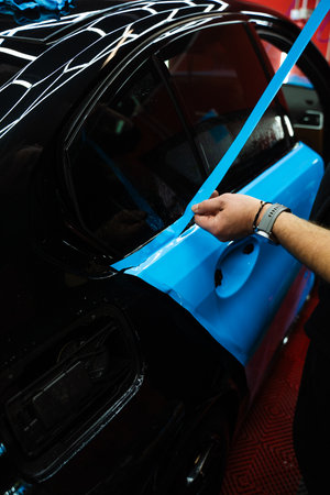 Precision PPF wrapping and detailing on car panel using sharp blade to trim wrap with accuracy. Car detailing involves precise vinyl cutting techniques. Precision cutting of PPF wrap on car bodyの写真素材