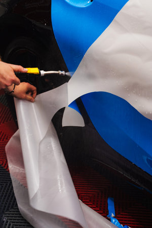 Paint Protection Film PPF Application Process. Detailer removes the liner from the PPF while applying water to the panel for clean adhesionの写真素材