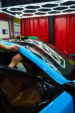 Detailing experts use hydration spray for controlled application of blue PPF film. Detailer uses spray-assisted method to apply vibrant blue vinyl wrap for perfect, bubble-free alignmentの写真素材