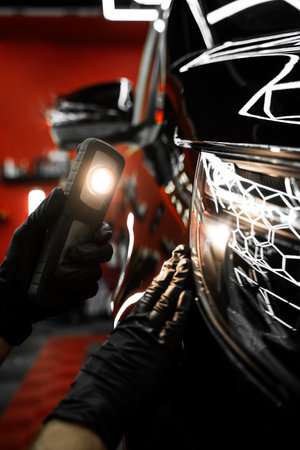 Swirl finder light to detect paint issues on black car in a detailing studio. Car Paint Inspection. Car paint inspection using detailing inspection light before polishing or ceramic coatingの写真素材