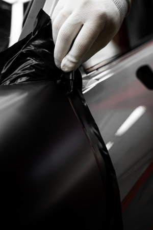Car wrap application changes vehicle appearance. Full Panel Car Vinyl Wrapping. Large-scale vinyl wrap installation transforms the vehicle exterior with matte black filmの写真素材
