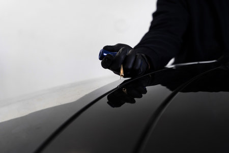 Windshield removal in progress using specialized cutting wire and scraper tool. Auto technician separates windshield using fine wire and scraping blade. Car windshield replacement processの写真素材
