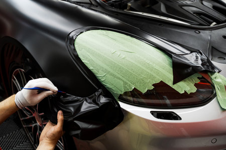 Trim tool to apply matte black wrap around a car panel edge. Car Wrapping with Trim Tool. Car detailing applies vinyl wrap around trim using plastic wedge tool for seamless finishの写真素材