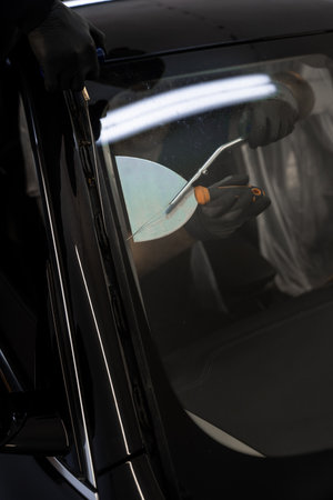 Car windshield replacement process. Windshield removal in progress using specialized cutting wire and scraper tool. Auto technician separates windshield using fine wire and scraping bladeの写真素材