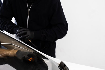 Auto technician separates windshield using fine wire and scraping blade. Car windshield replacement process. Windshield removal in progress using specialized cutting wire and scraper toolの写真素材