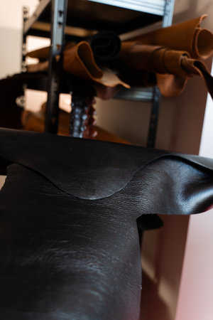 Leather Hide Selection in Workshop. Rolled hides in varied tones and grains emphasize diversity,...