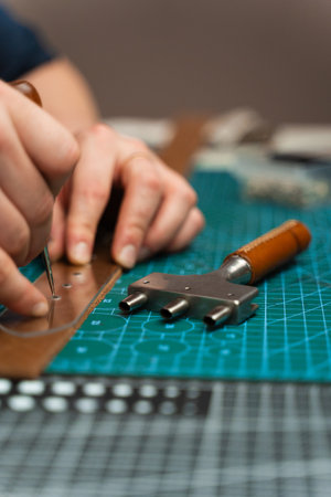 Punching and detailing leather belt holes. Artisan punching holes into a leather strap for a...