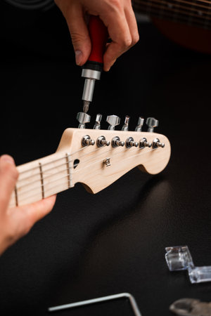 Guitar Repair with Screwdriver and Tools. Musician repairs guitar headstock with precision tools, tightening tuning pegs. Guitar headstock is carefully adjusted with a screwdriverの写真素材