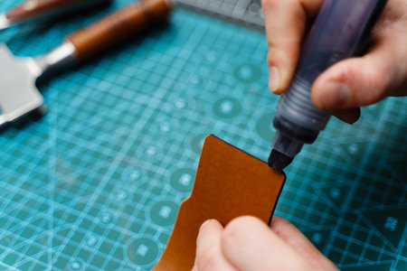 Edge finishing with dye marker. Artisan applies edge dye to leather piece, enhancing durability....