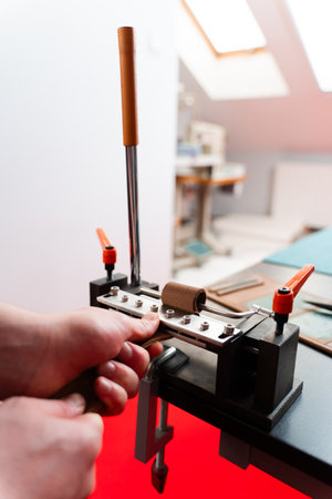 Leatherworker uses a creasing press to refine strap edges, adding detail and smoothness for...