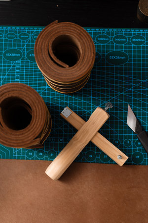 Leather rolls and strap cutter lie on cutting mat, ready for trimming strong belts and leather goods. Sharp strap cutter and leather rolls, essential for crafting accurate belt strapsの写真素材