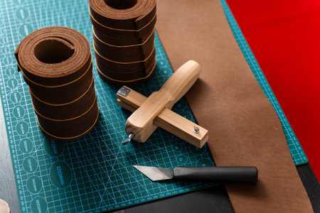 Leather rolls and strap cutter lie on cutting mat, ready for trimming strong belts and leather goods. Sharp strap cutter and leather rolls, essential for crafting accurate belt strapsの写真素材