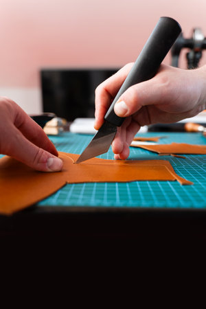 Craftsman prepares leather pieces by cutting with precision, ensuring accurate templates for leather handmade goods. Cutting leather with knife. Craftsman carefully cuts leather with precision toolsの写真素材