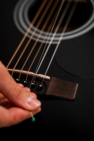 Acoustic guitar string replacement in progress. Guitarist stretches new strings onto the fretboard. Installing new guitar strings. Musician installing a new string on an acoustic guitarの写真素材