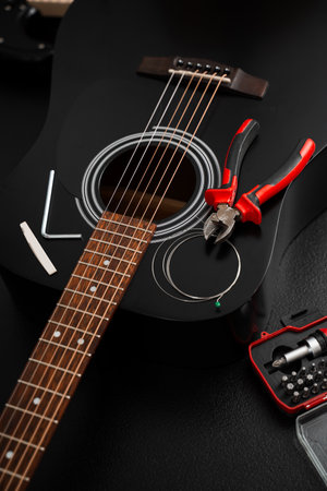 Guitar string replacement with tools. Acoustic guitar setup in progress with new strings and essential tools on the table. Restringing process with pliers and screwdriver kit near acoustic guitarの写真素材