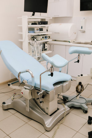 Woman seated in gynecology chair before examination. Modern gynecological chair and microscope ready for gynecology exam. Girl awaits consultation in a gynecological office with specialized toolsの写真素材