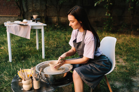 Girl shapes clay on the pottery wheel with smile. Young woman smiling while working with clay on pottery wheelの写真素材