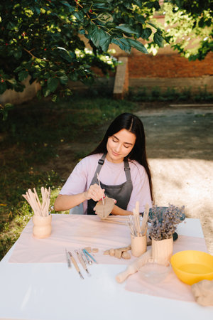 Woman Carving Clay Leaf. Young woman carves delicate leaf patterns into clay, showcasing her pottery skills. Artisan engraves a clay leaf with detailed linesの写真素材