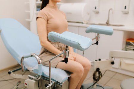 Woman seated in gynecology chair before examination. Modern gynecological chair and microscope ready for gynecology exam. Girl awaits consultation in a gynecological office with specialized toolsの写真素材