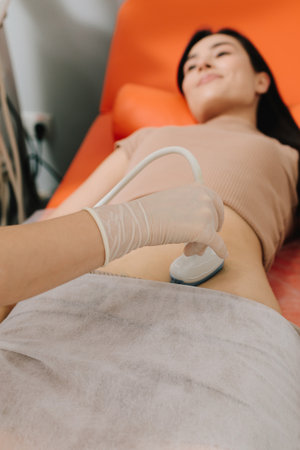 Abdominal ultrasound. Gynecologist uses ultrasound equipment for reproductive health evaluation. Gynecologist performs an abdominal ultrasound on a relaxed patientの写真素材