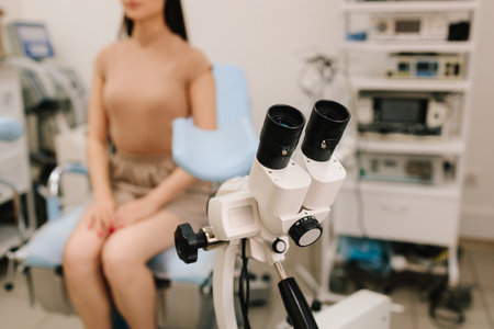 Woman seated in gynecology chair before examination. Modern gynecological chair and microscope ready for gynecology exam. Girl awaits consultation in a gynecological office with specialized toolsの写真素材