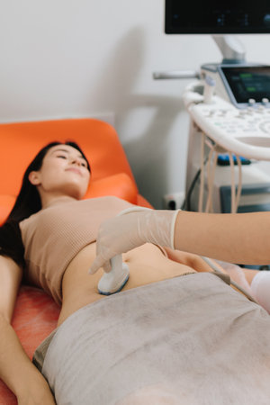 Gynecologist performs an abdominal ultrasound on a relaxed patient. Abdominal ultrasound. Gynecologist uses ultrasound equipment for reproductive health evaluationの写真素材