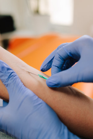 Insert a needle for blood collection close-up. Nurse in sterile gloves performs a venipuncture,...