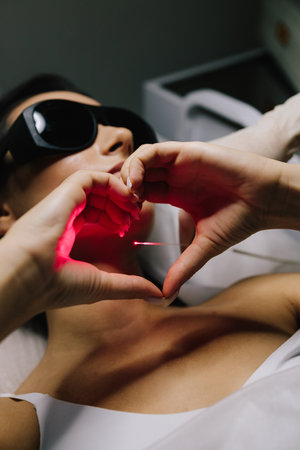 Girl shows love to laser procedure using hands. Aesthetic laser therapy removes benign nevi and vascular lesions. Laser coagulation procedure for nevus elimination and vascular lesion correctionの写真素材