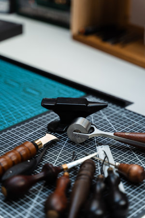 Traditional wooden-handled awls and cutters beside a small anvil illustrate timeless craftsmanship and dedication to bespoke design. Leathercraft Tools on Workbenchの写真素材