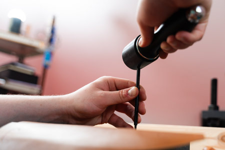 Punching leather hole with mallet and chisel. Precision leatherwork involves punching holes with a...