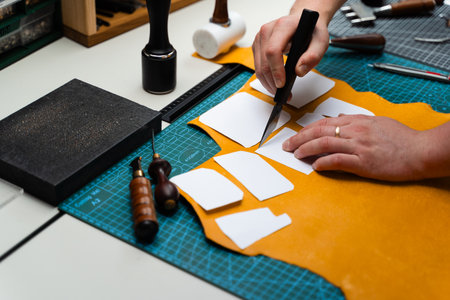 Leather Cutting with Knife and Templates. Artisan cuts premium leather with sharp knife and paper...