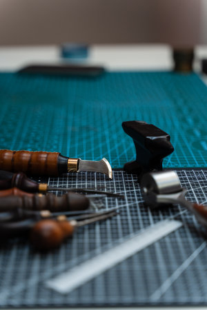 Traditional wooden-handled awls and cutters beside a small anvil illustrate timeless craftsmanship and dedication to bespoke design. Leathercraft Tools on Workbenchの写真素材